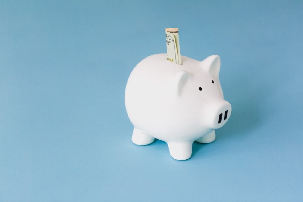 A white piggy bank with a dollar sticking out of it.