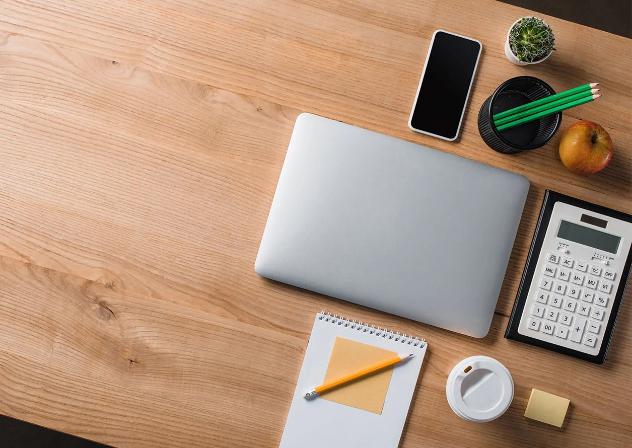 Overhead view of a wooden desk with a laptop and office supplies on it.