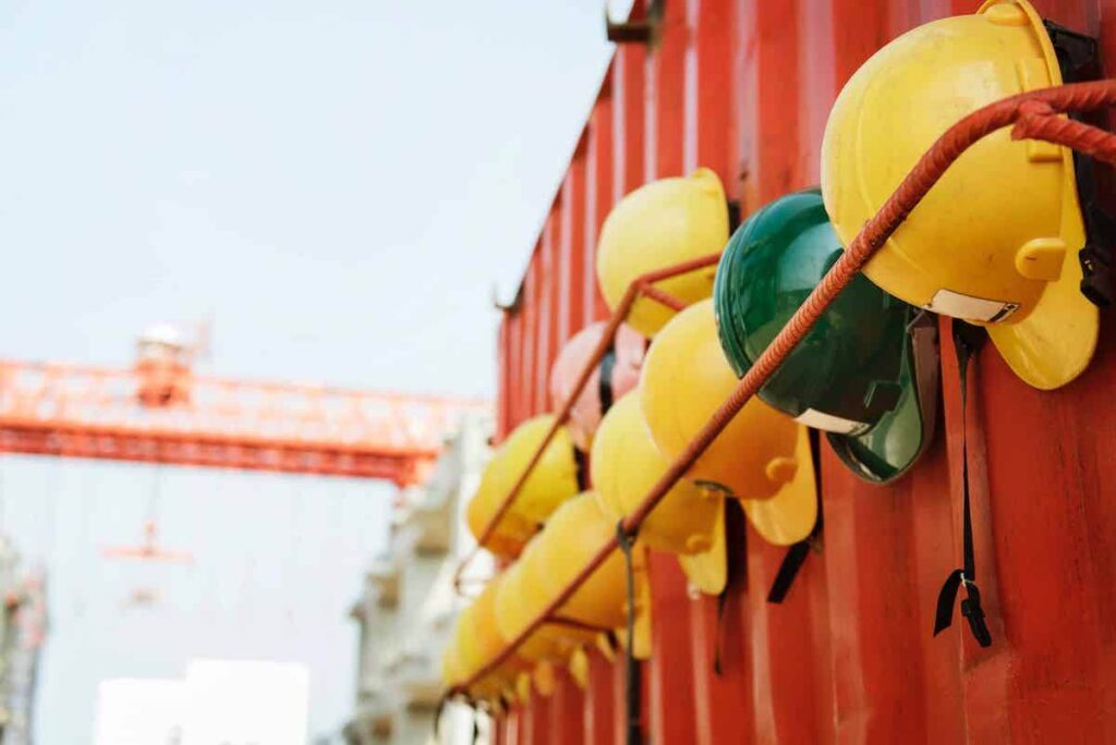 Yellow hard hats (save for one green one) hanging on the side of a metal container.