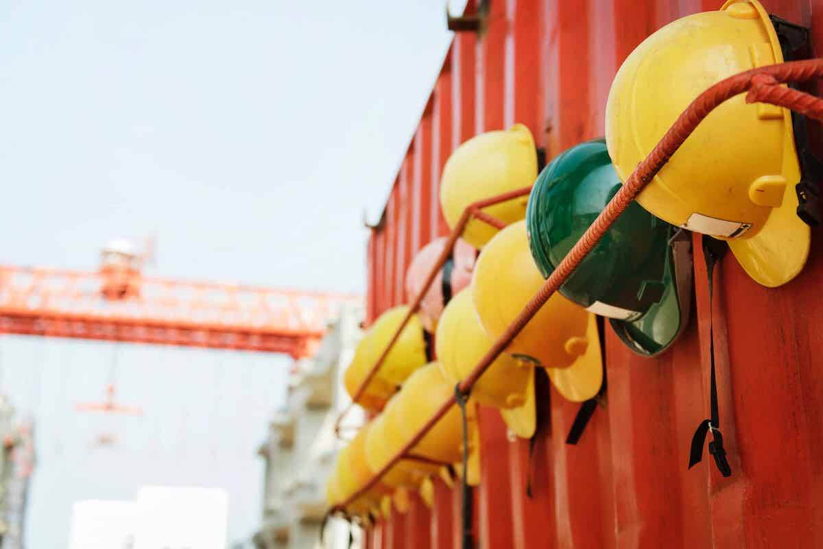 Yellow hard hats (save for one green one) hanging on the side of a metal container.