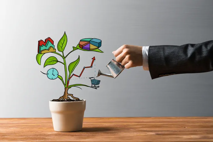 Businessman hand holding watering can over cartoon plant containing symbols that represent business growth