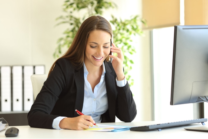 Happy businesswomen talking on cell phone and taking notes at a desk in an office