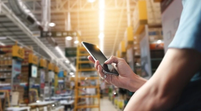 Man's hand using smartphone in large warehouse