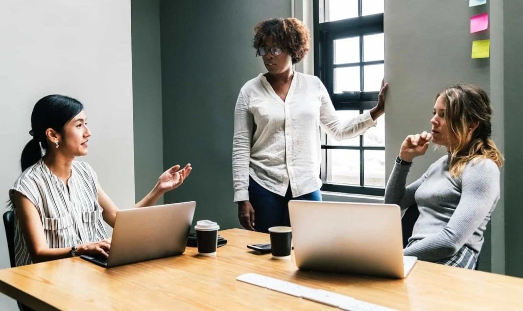 Three diverse women at a conference table in a work meeting