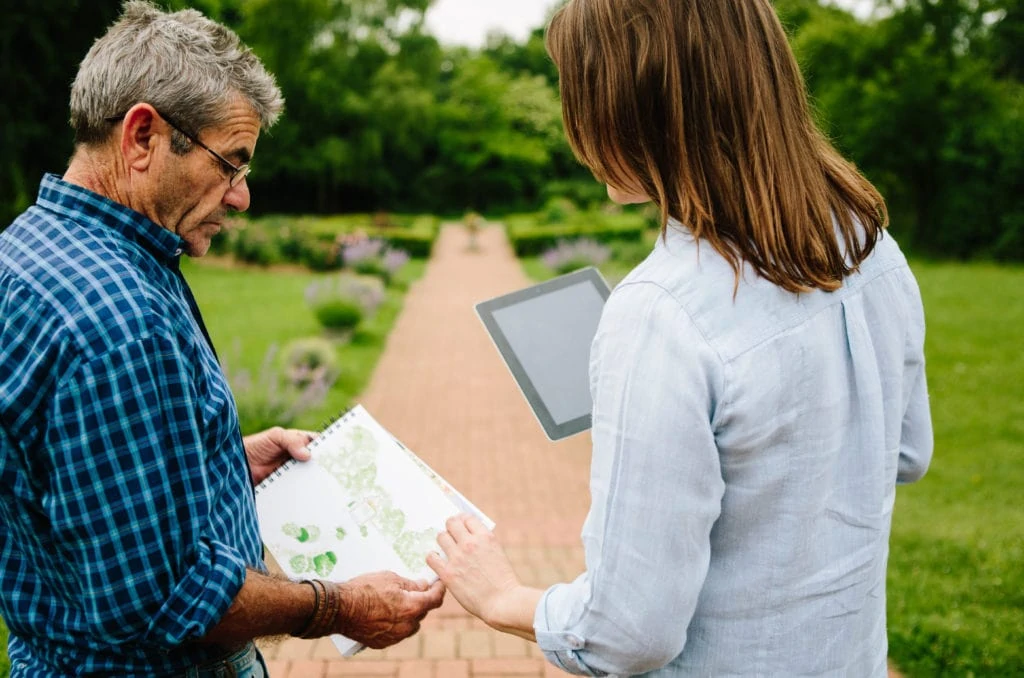 Two Gardeners At Work Checking Plans For A Formal Garden