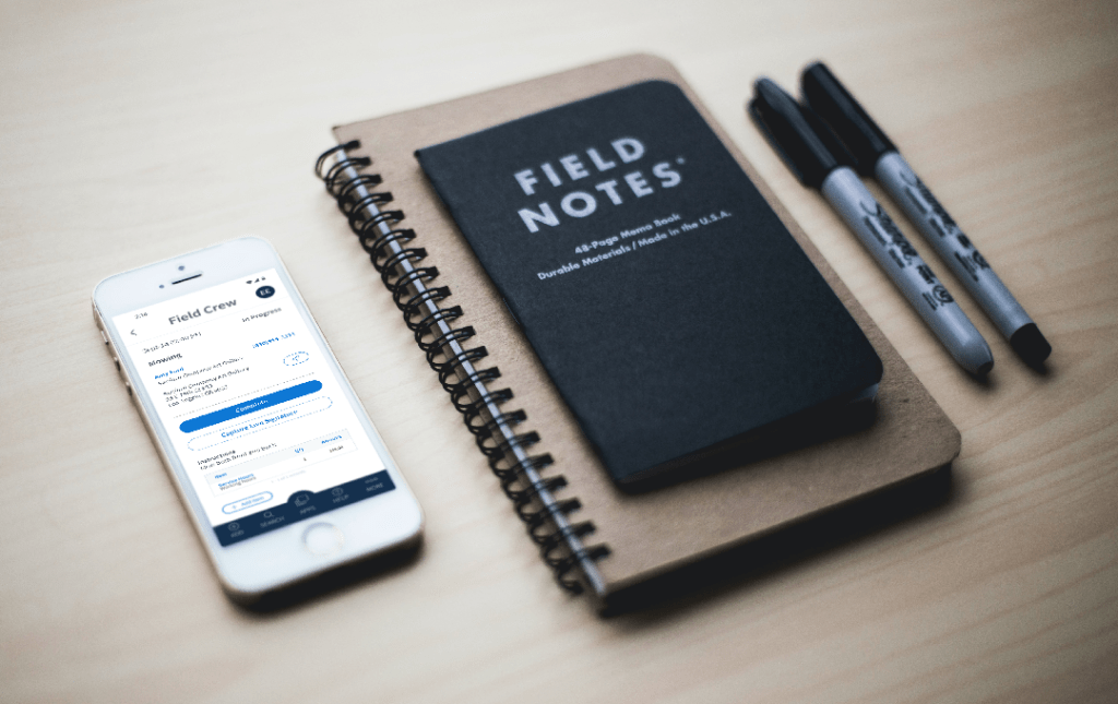 Method:Field Services mobile app on a white iPhone alongside a black field notes notebook and two black Sharpie markers.