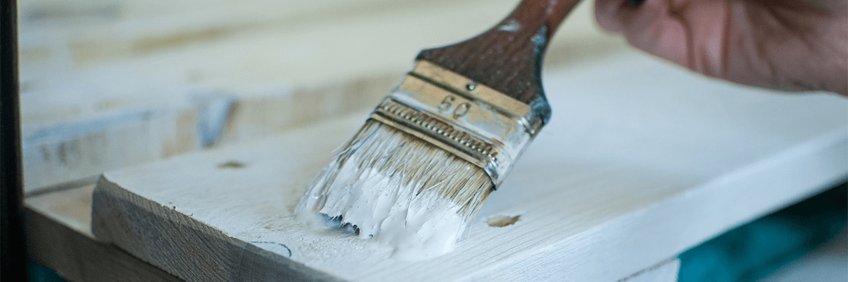 Paintbrush with white paint on it being used to paint a bench. Or something.