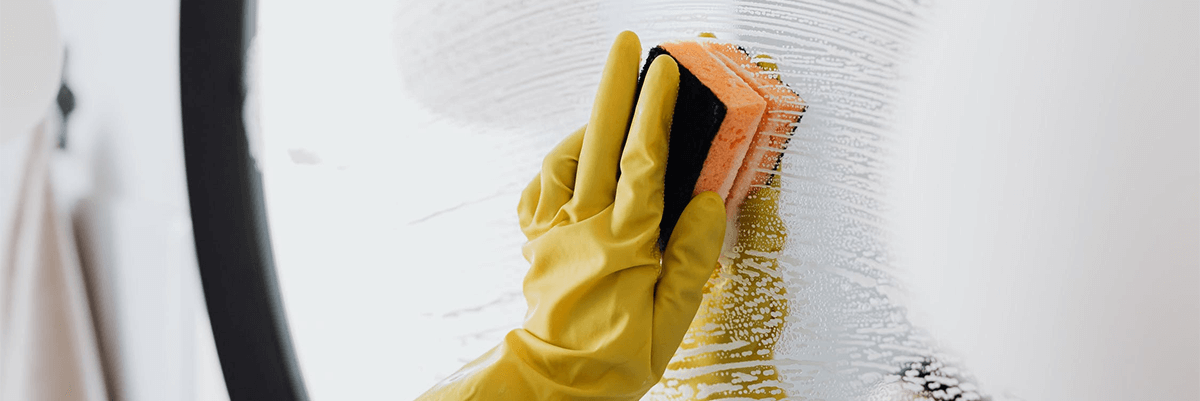 Gloved hand scrubbing a mirror with a sponge.