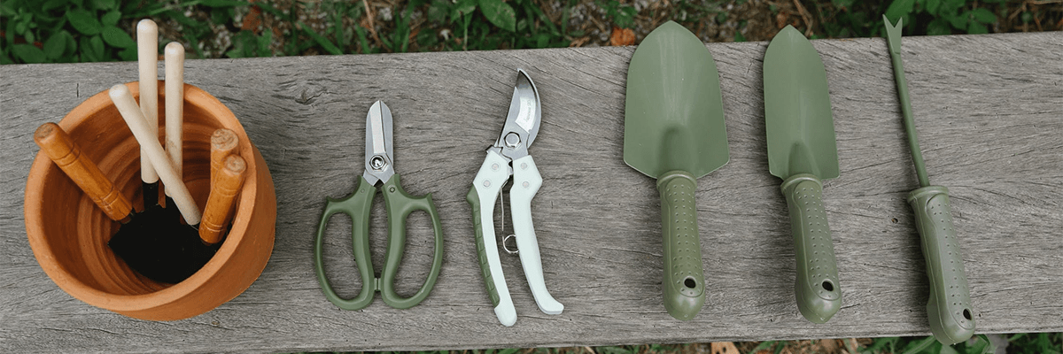 A variety of gardening tools, like scisssors and trowels, on a wooden board.