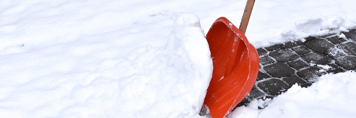 A red snow shovel shovelling snow on a cobble stone sidewalk.