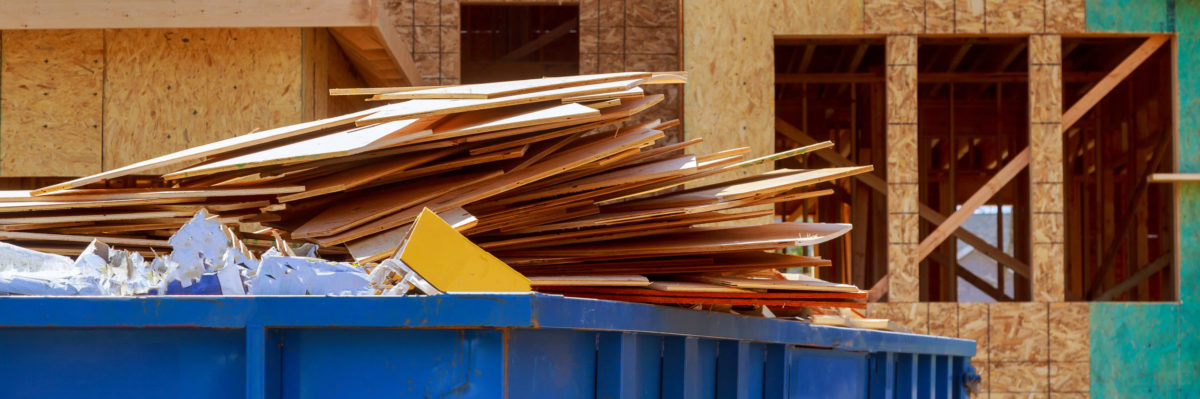 Large blue garbage bin with plywood in it at a construction site.