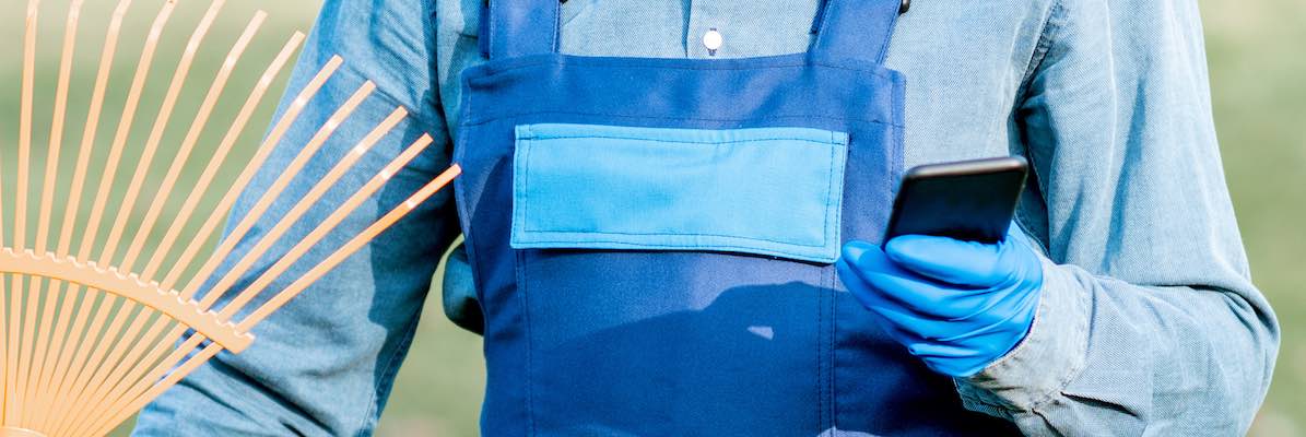 Professional sweeper in uniform using phone during the work in the garden