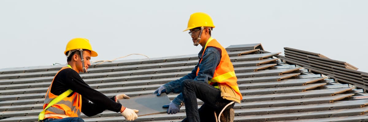 Construction worker wearing safety harness belt during working installing concrete roof tile on top of the new roof