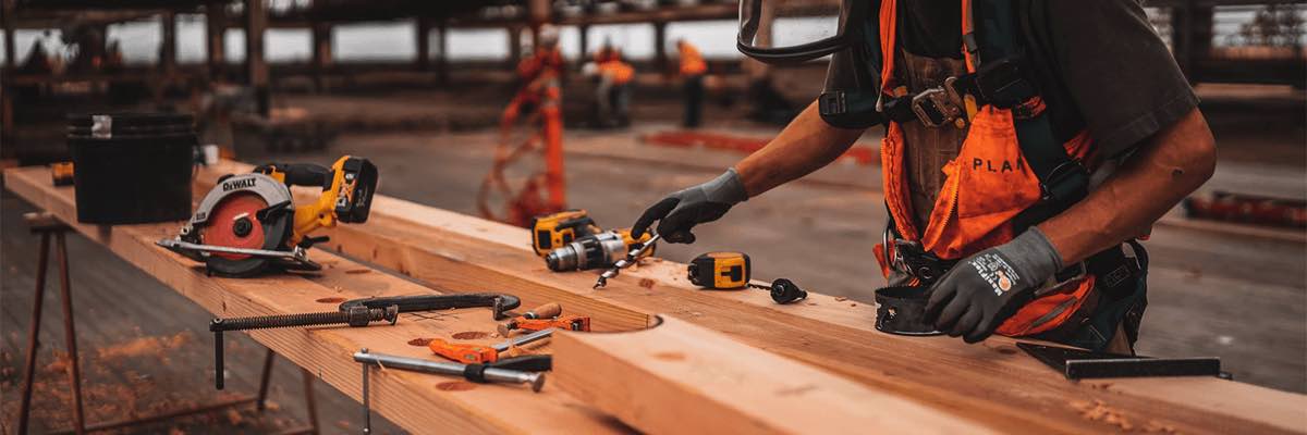 man in orange and black vest wearing white helmet working with wood