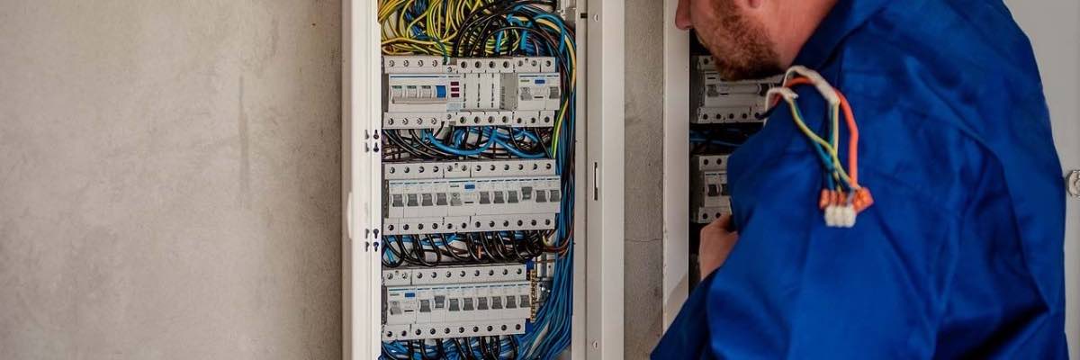 Electrician in blue uniform looking at electric panel