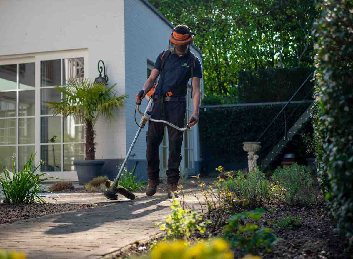 man in black t-shirt and blue denim jeans holding weed whipper