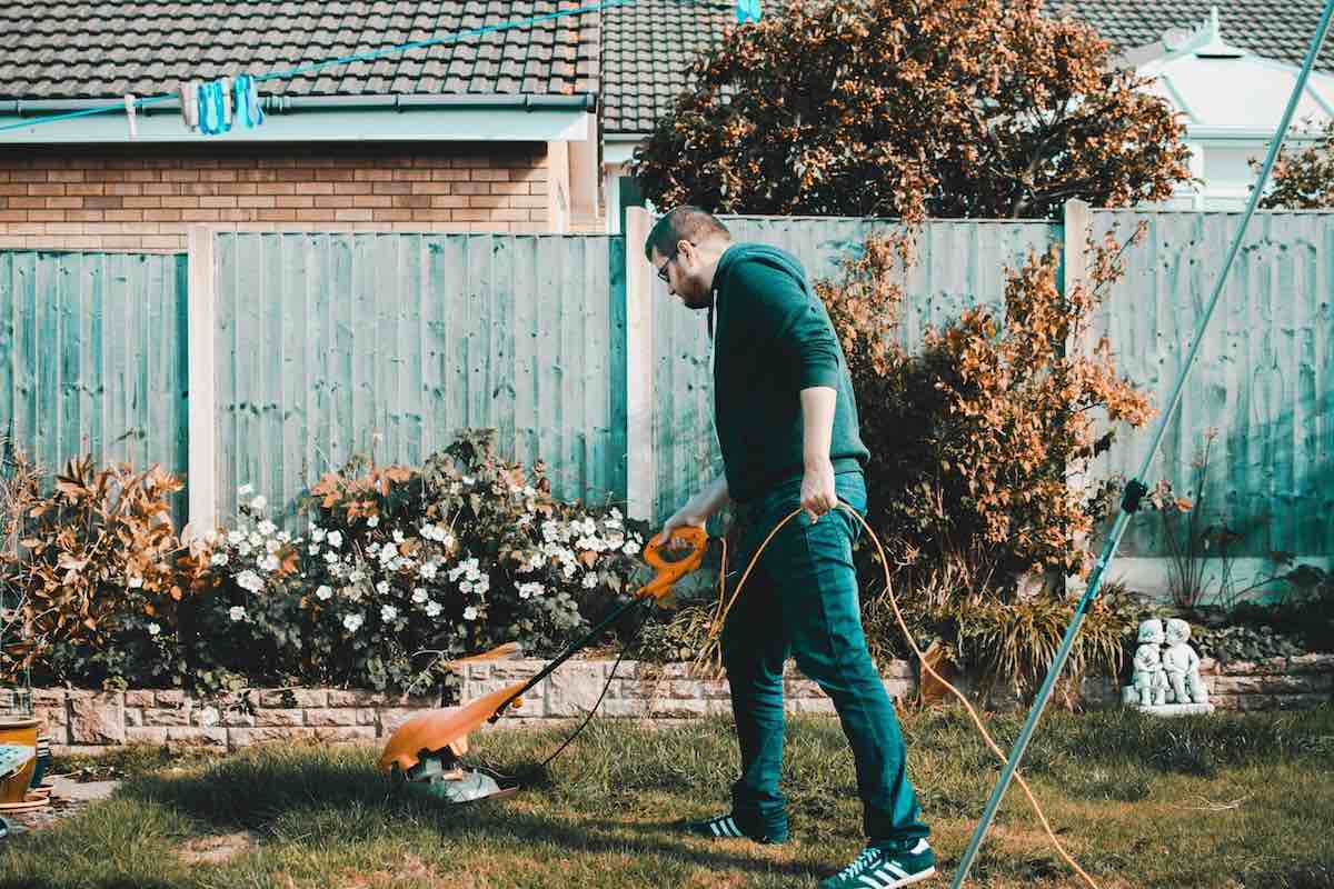 man with hoodie and glasses using a weedwhipper to wheedwhip