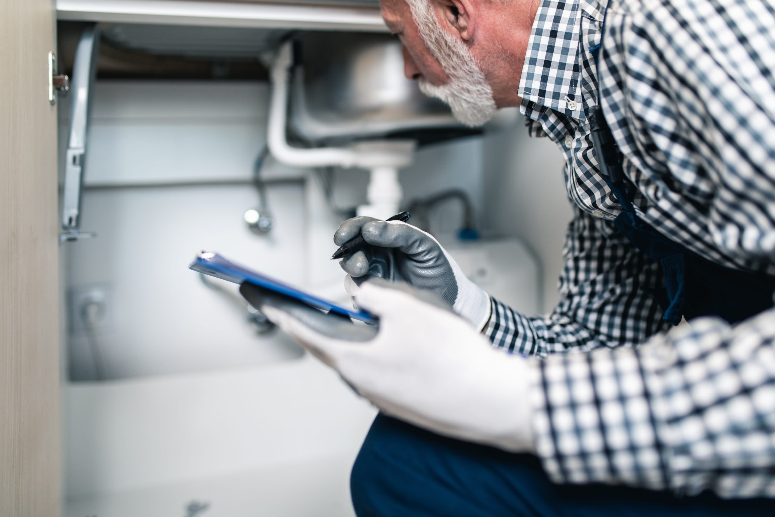 Senior man plumber working with plumbing tools on the kitchen. R