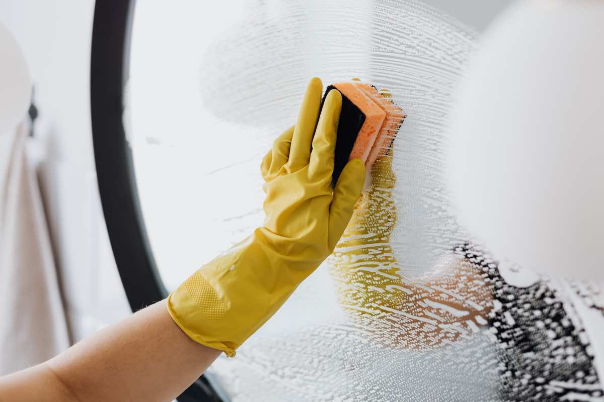 Hand in a rubber glove cleaning a mirror with a sponge