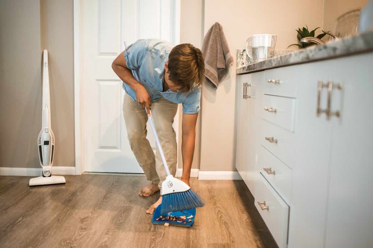 A person sweeping up what looks like wood shavings in the most awkward position possible