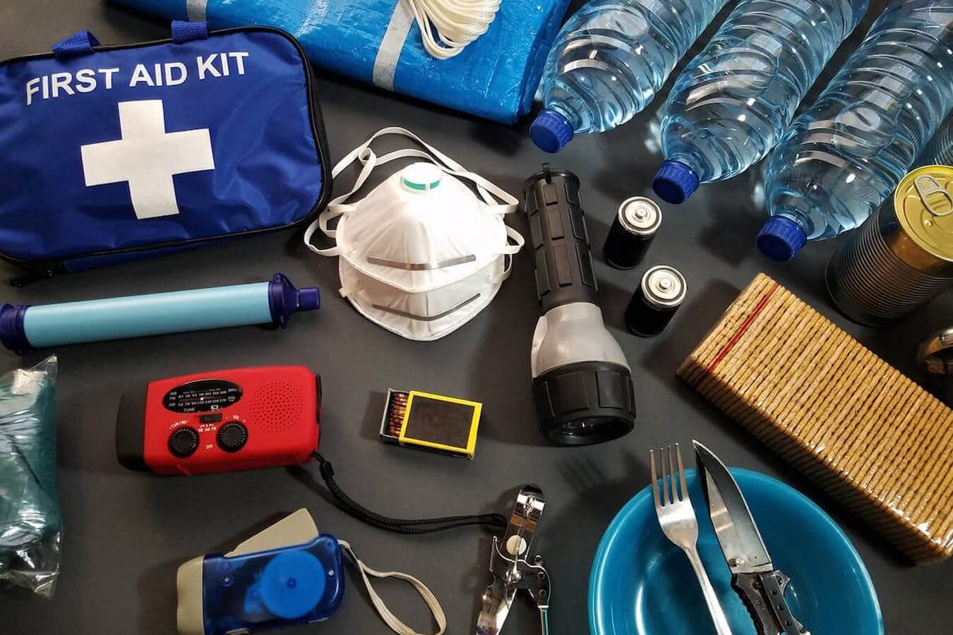 A variety of emergency preparedness supplies, like a first-aid kit, cans of food, matches, flashlights, etc.
