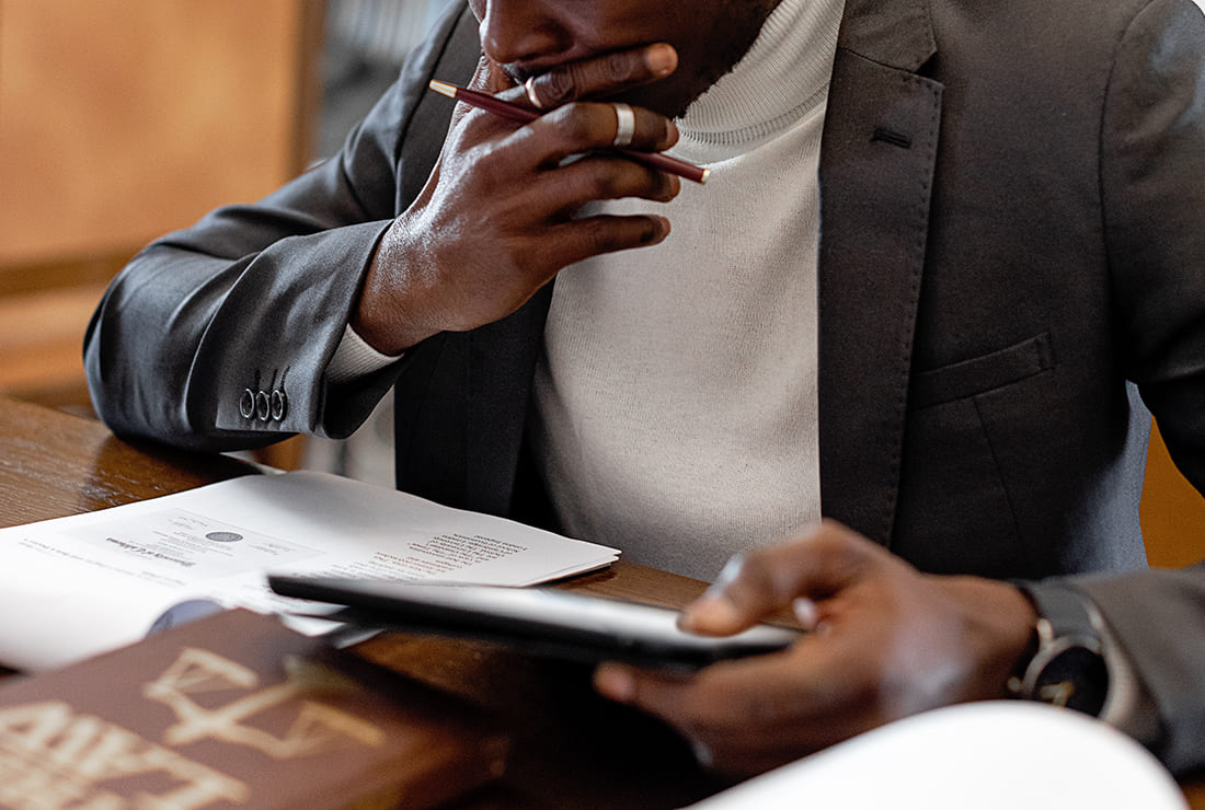 This image shows a pensive man holding a tablet and looking down at paper documents.