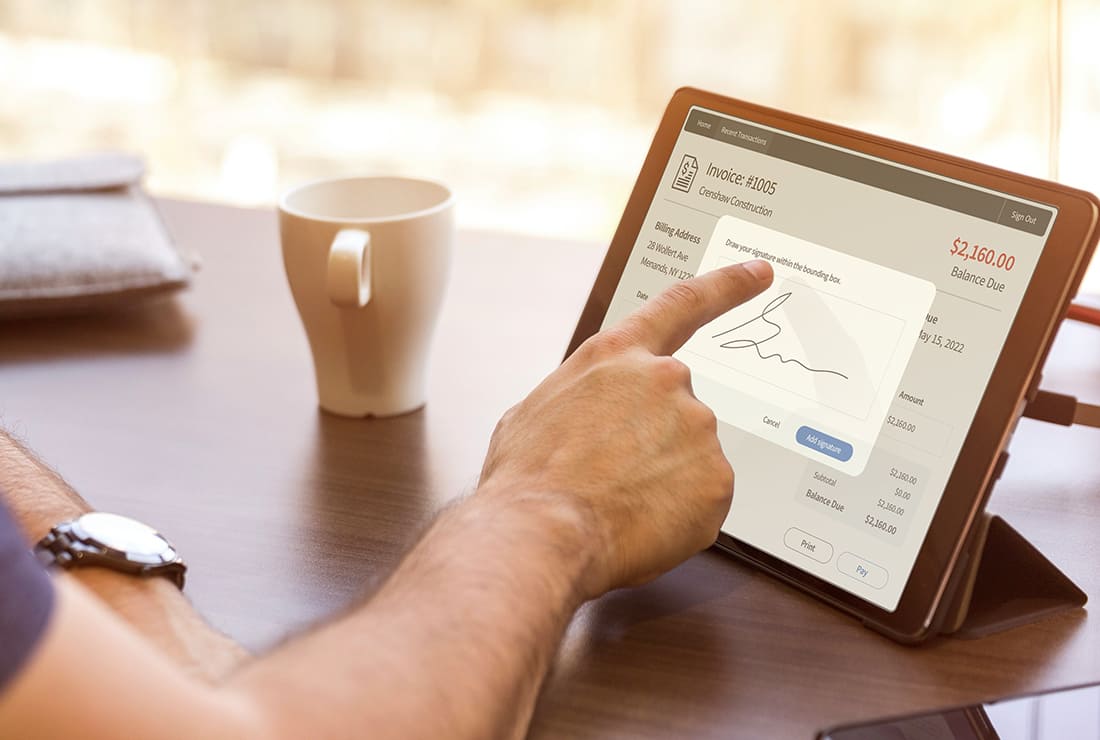 This image shows a man sitting at a desk in front of a tablet device. We can see him digitally signing an invoice on the tablet screen.