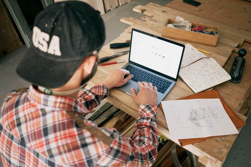 man in a backwards-hat and plaid shirt typing on a laptop.