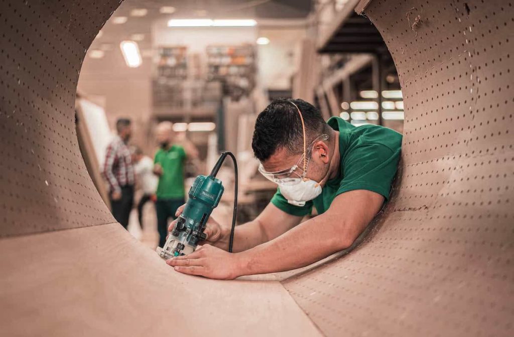 Men in green shirts wearing masks. One is sanding.