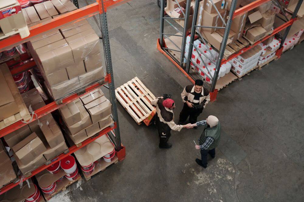 men in a warehouse, surrounded by boxes on shelves.