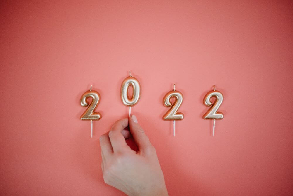 a hand placing gold candles that read '2022' against a pink background.