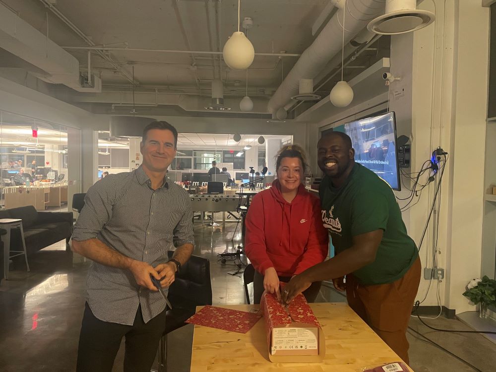 Method team wrapping Christmas gifts in an office and smiling at the camera. 