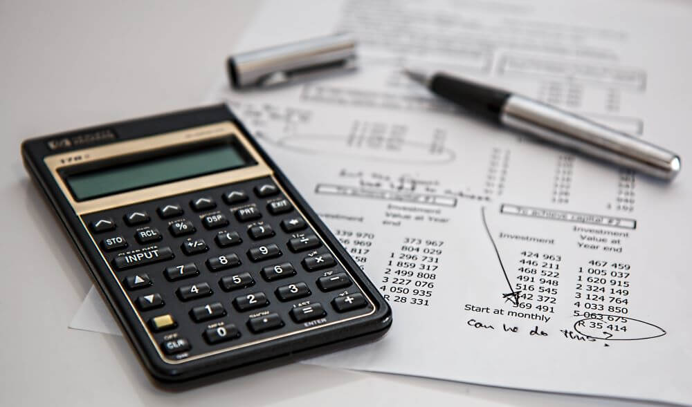 a black calculator near a ballpoint pen on a paper with calculations on it