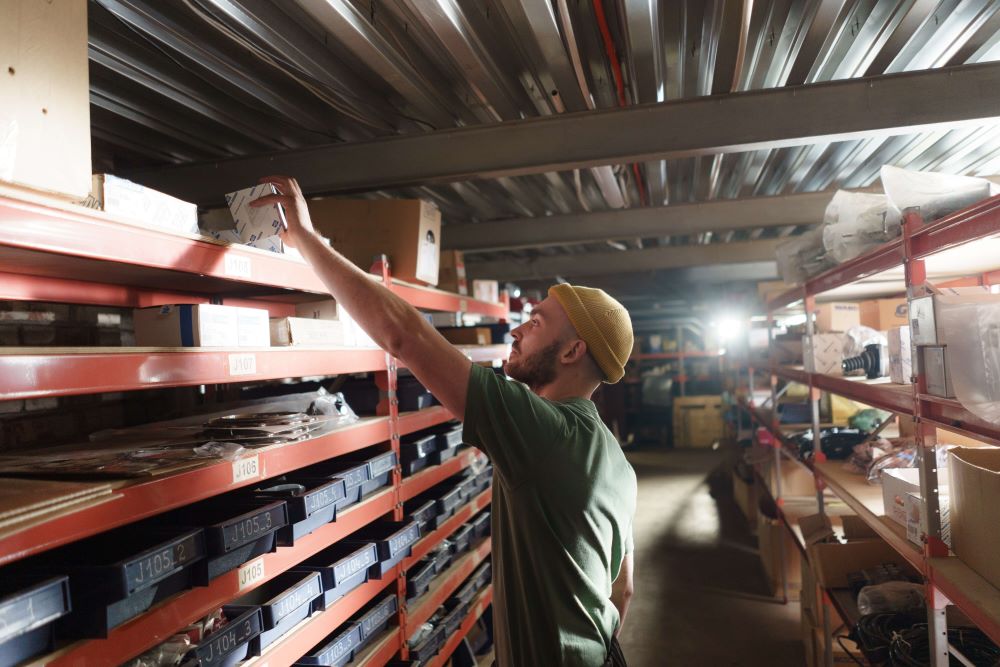 man in a knit hat reaching over to place a product on a top shelf.