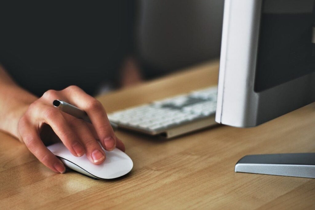 Closeup of hand holding pen and clicking mouse in front of computer