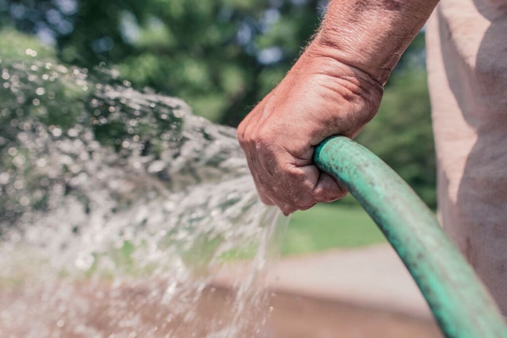 Man's hand holding garden hose that is spraying water