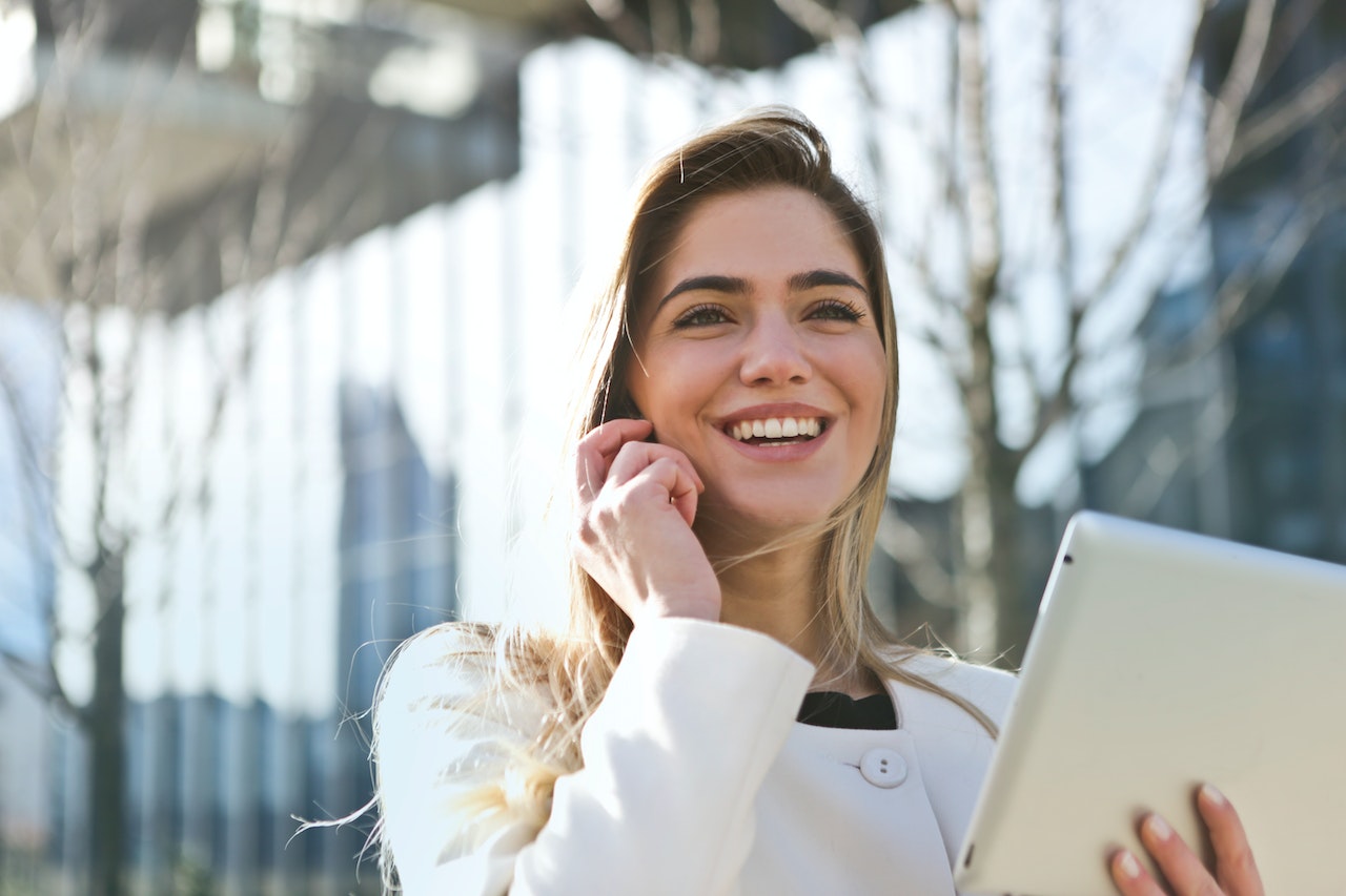 This image shows a woman smiling while talking on the phone and holding a tablet.