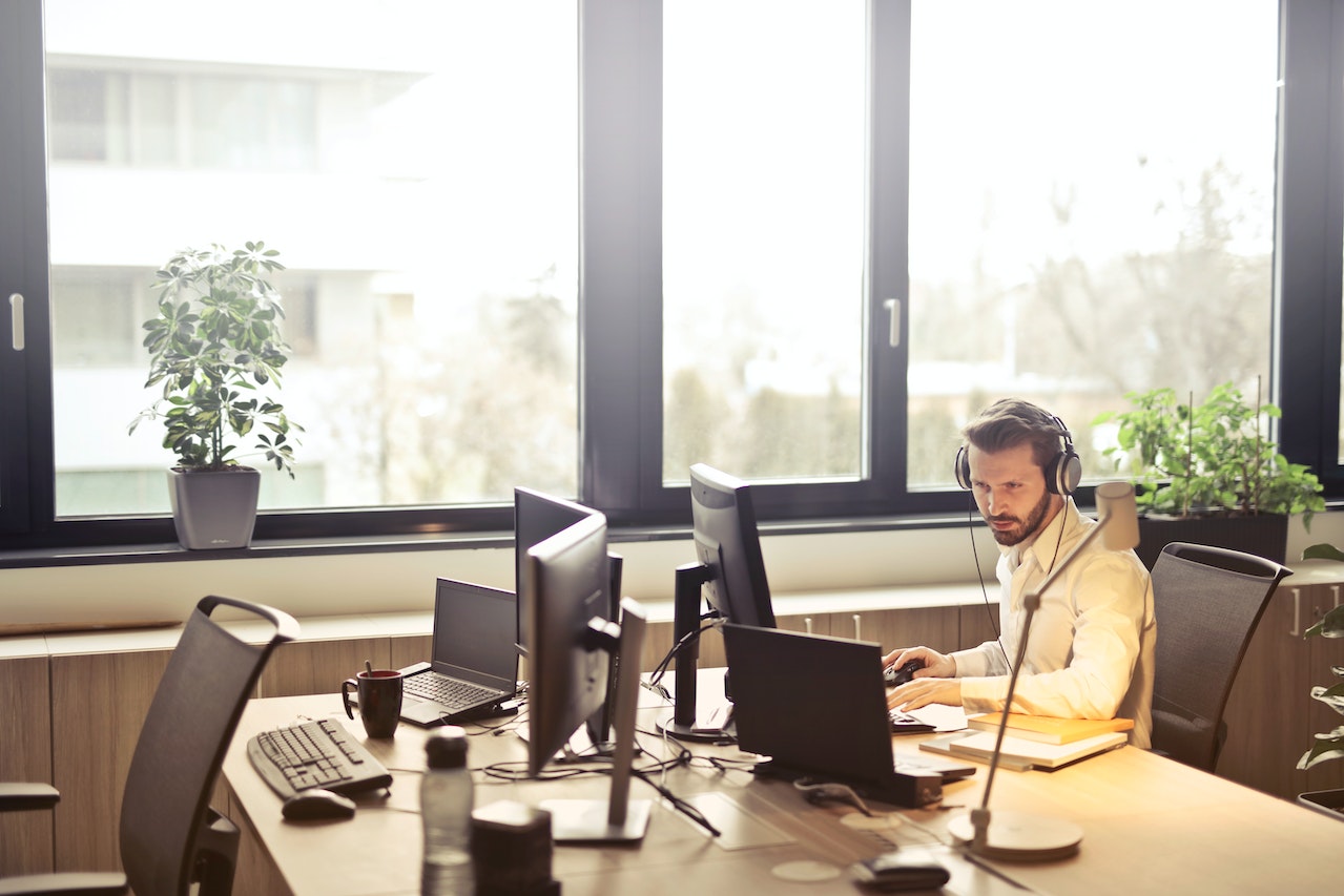 This image shows a man wearing a headset sat a desk working on his computer.