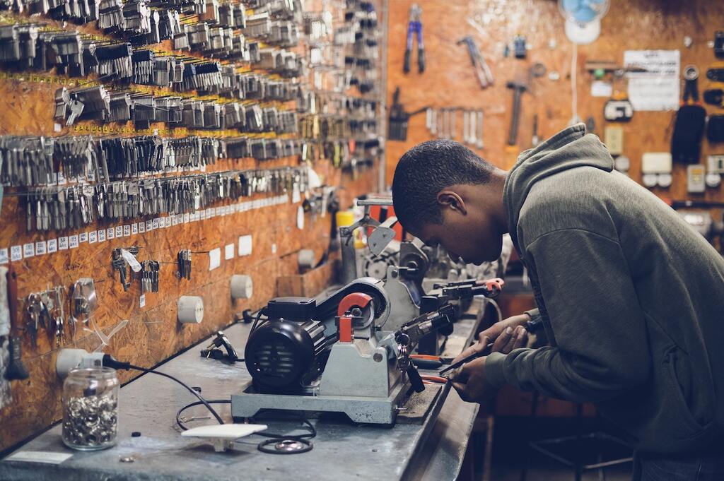 This image shows a man hunching over a work table molding a copy of a key.