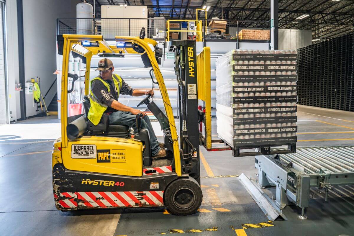 A man backs up a forklift in front of slats.