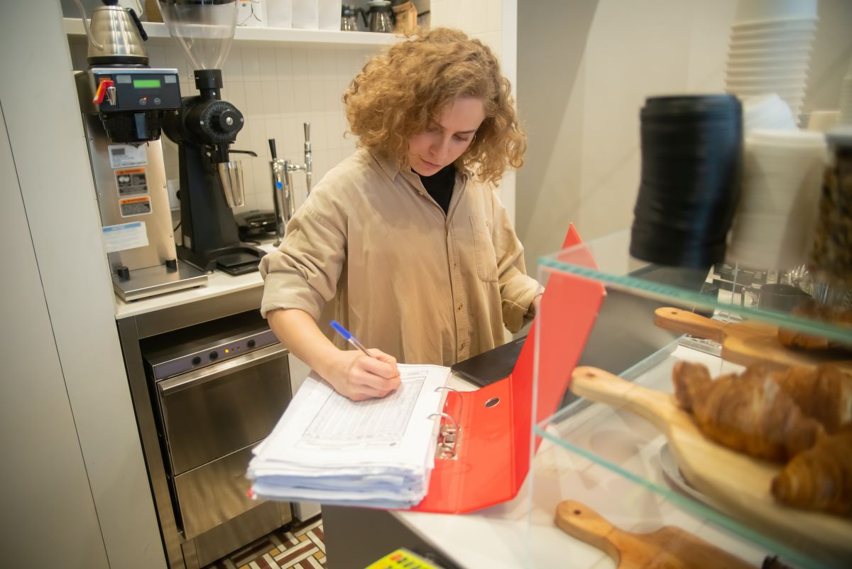 A woman filling out inventory in a coffee shop.