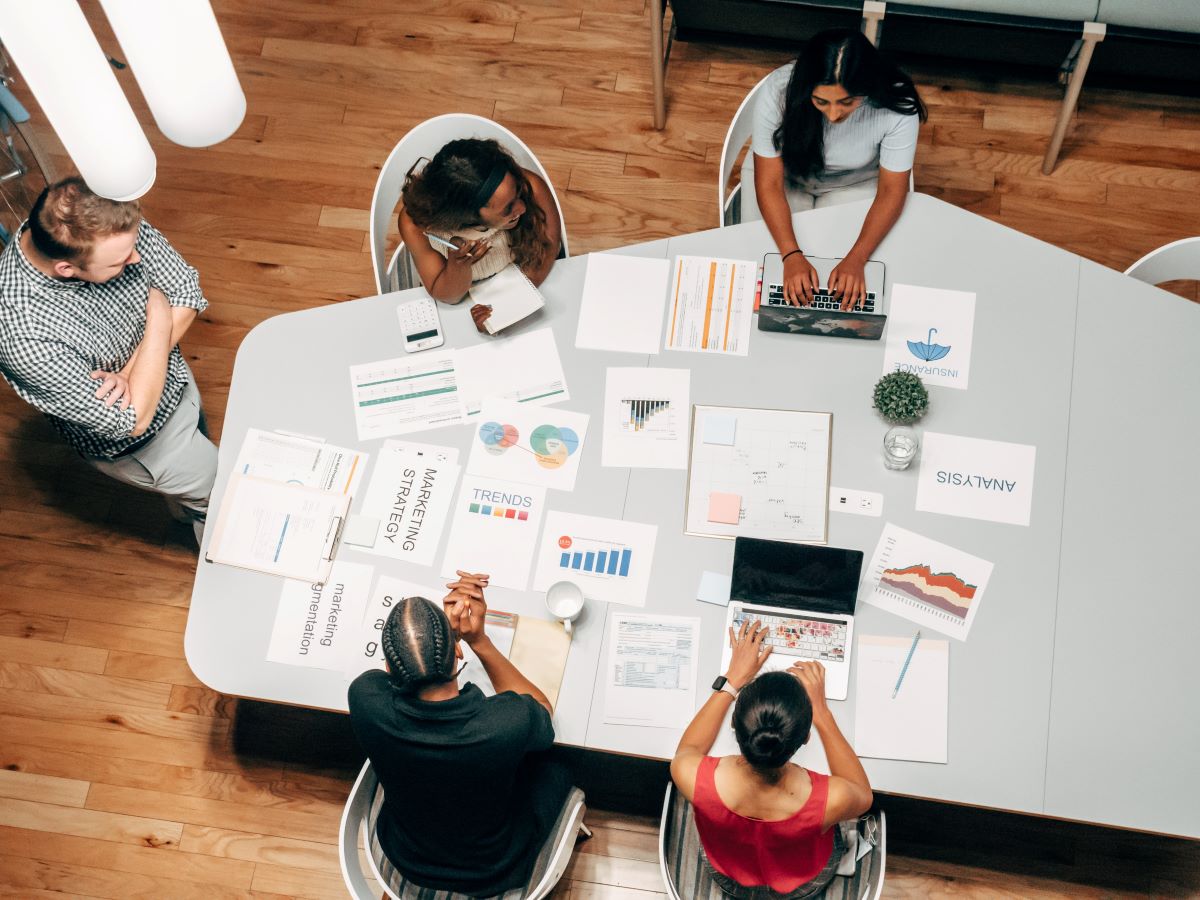 Bird's eye view of people sitting around a cluttered table discussing a project.