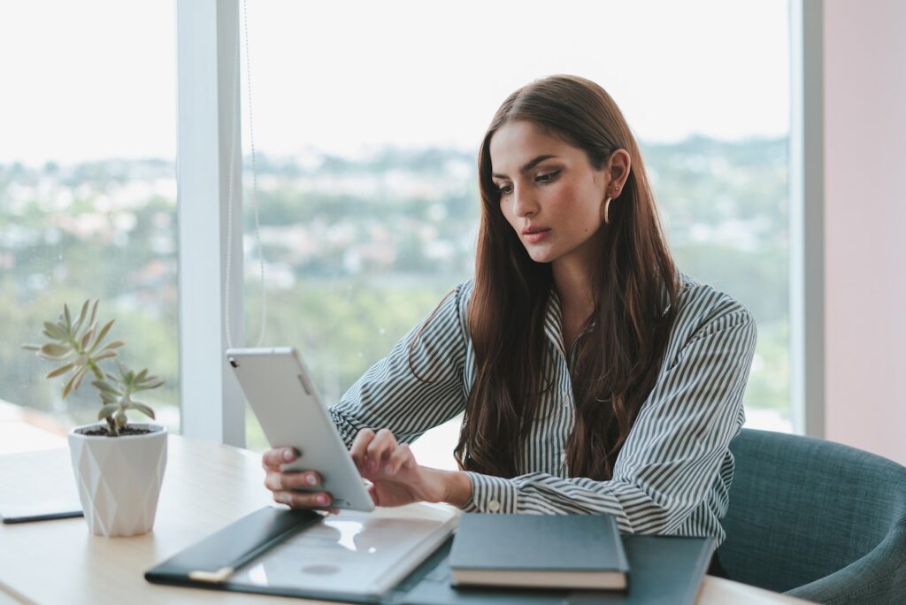 This image shows a woman at a document-filled desk looking at a tablet.