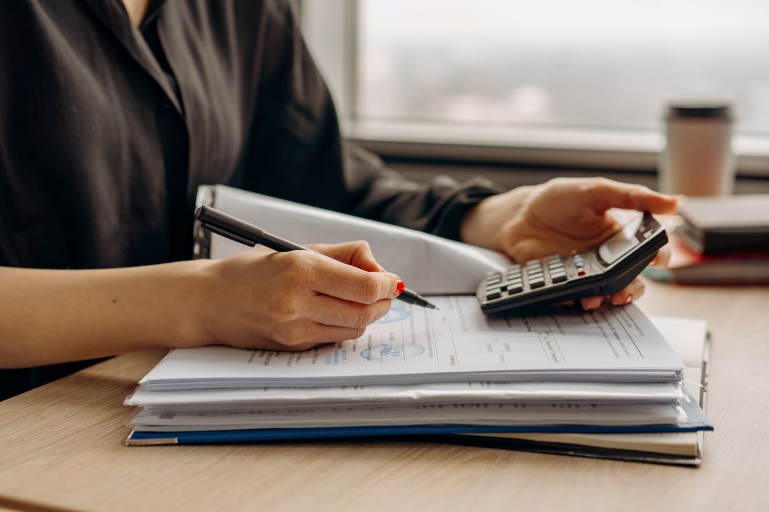 A woman holding a calculator and filling out a form with a pen.