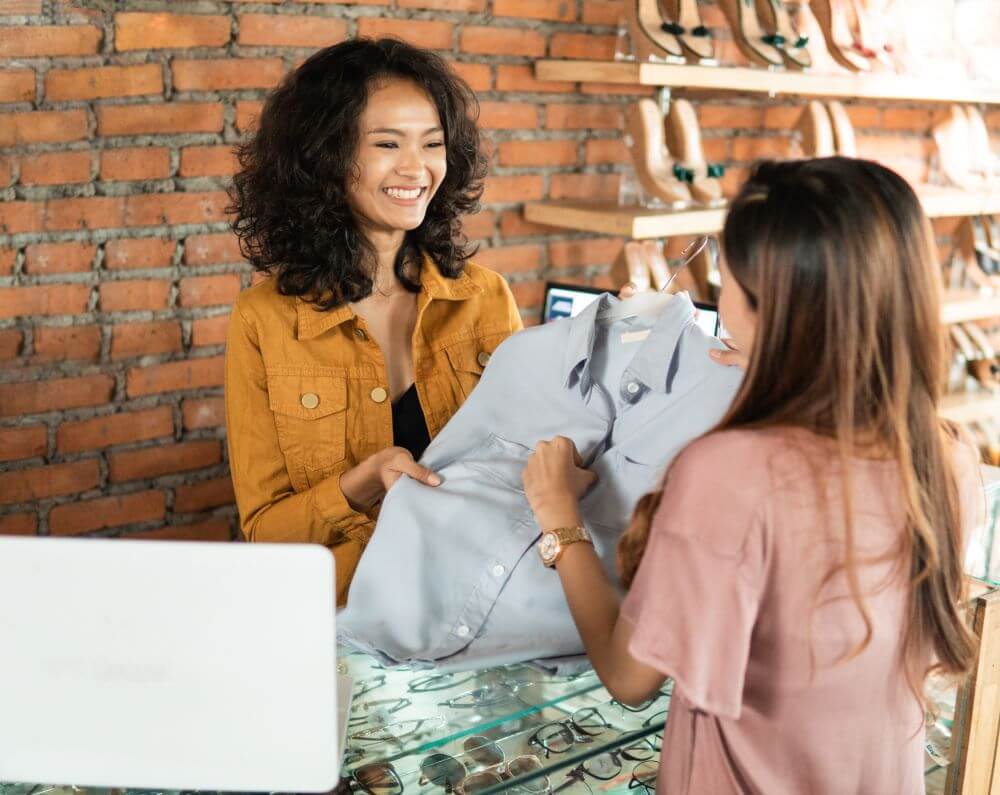 A store employee handing over a clothing item to a customer while smiling