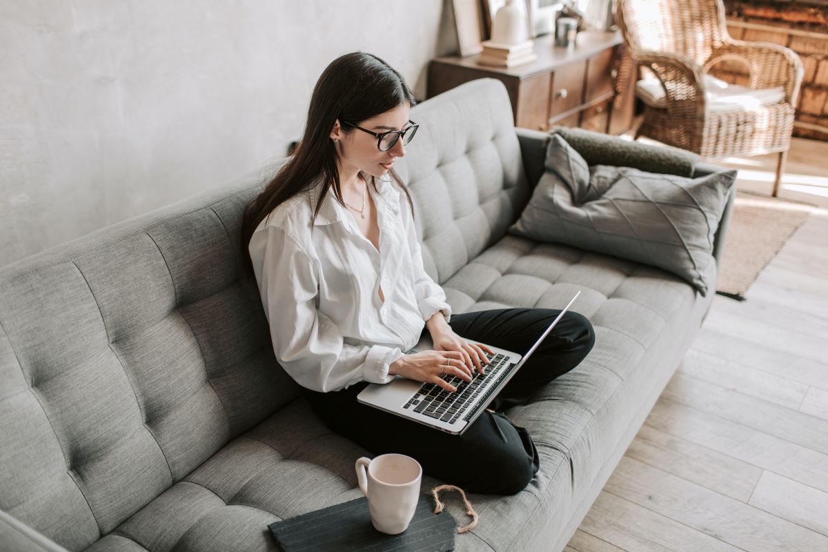 A woman sitting on a couch working on her laptop with a cup of coffee beside her.
