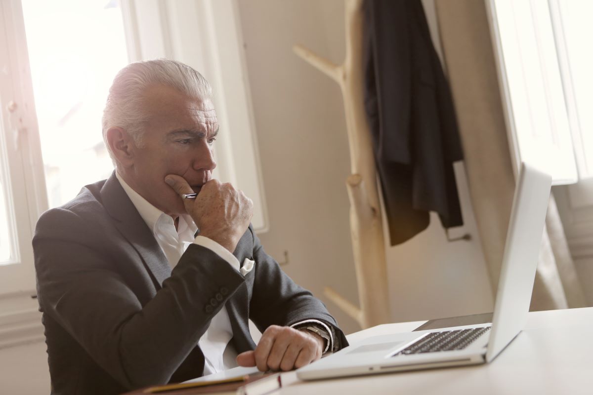 An older man sitting at a desk, looking focused on his laptop.