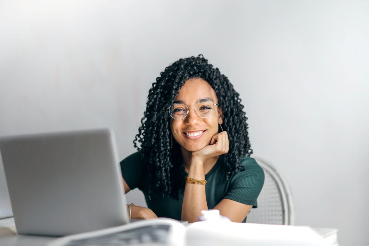 a woman on her laptop smiles and looks into the camera