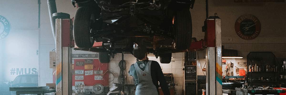 Repair person underneath a raised car in an auto shop