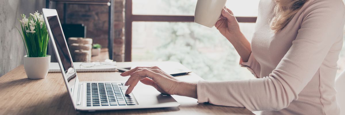 Concept of having a workplace at home. Side profile half-faced photo of happy cheerful smiling excited woman drinking coffee and typing a letter on computer